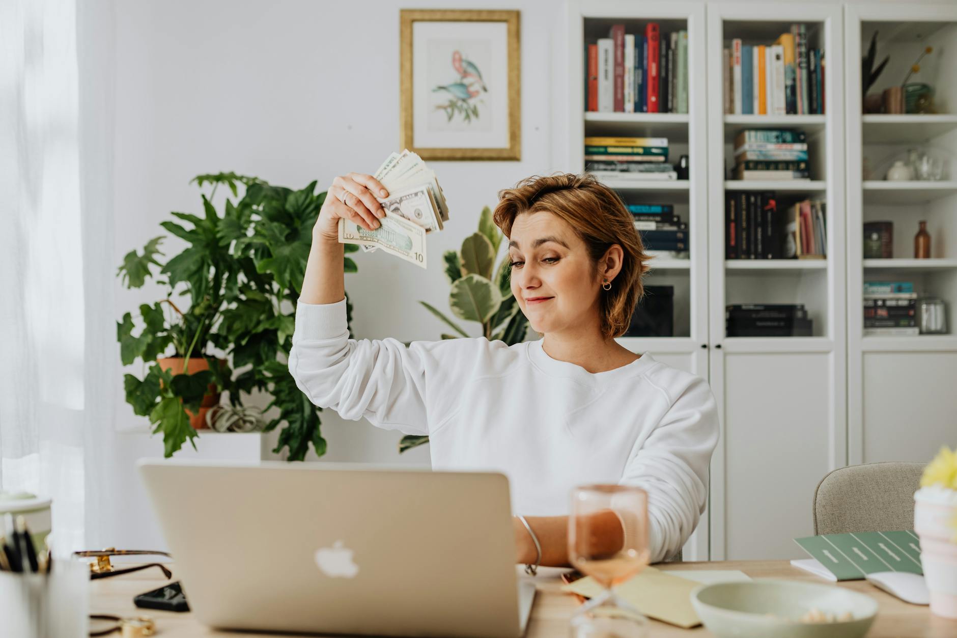 woman sitting in an office in front of a laptop and waving cash